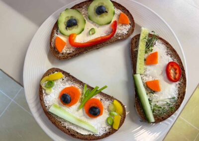 Teller mit 3 belegten Brotscheiben mit lustigen Gesichtern aus Gemüse.