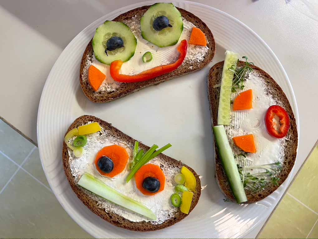 Teller mit 3 belegten Brotscheiben mit lustigen Gesichtern aus Gemüse.
