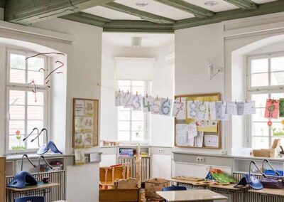 Blick in ein Klassenzimmer mit Tischen und Stühlen, großen Fenstern und Deko