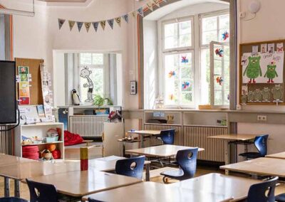 Blick in ein Klassenzimmer mit Tischen und Stühlen, großen Fenstern und Deko